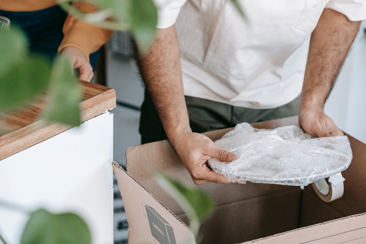 Man preparing dishes in a box for moving into a new home during the day.